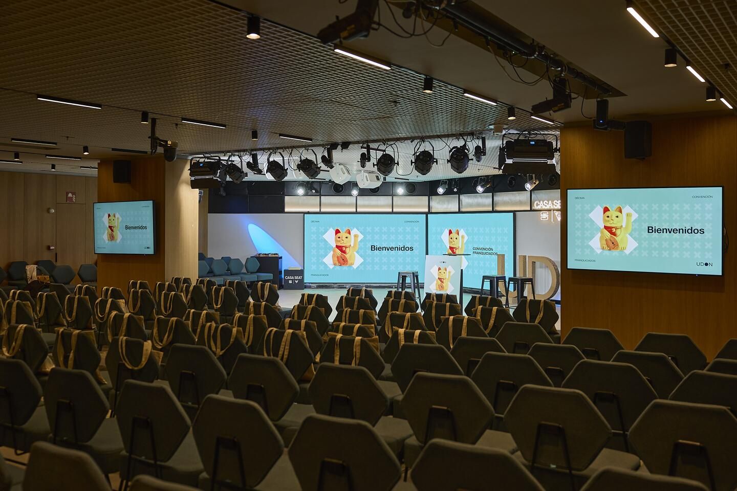 Overview of the auditorium at Udon's Franchisee Convention, with welcome bags on every chair and the event graphics on the screens