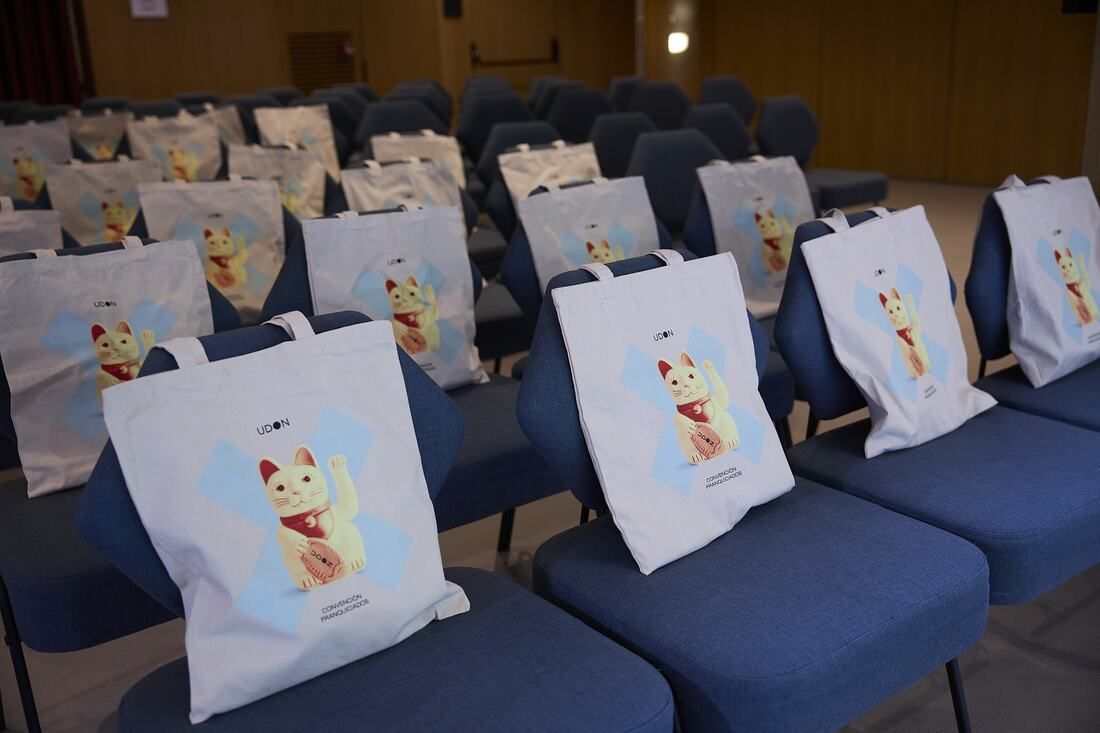 Tote bags featuring the lucky cat and the X, laid out on the chairs for each franchisee